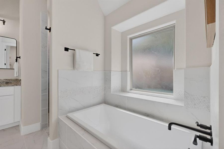 Alcove bathtub with matte black fixtures and a window with privacy glass