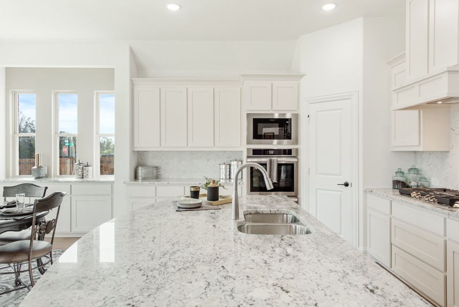 White kitchen with granite island, stainless steel appliances, and built-in double oven