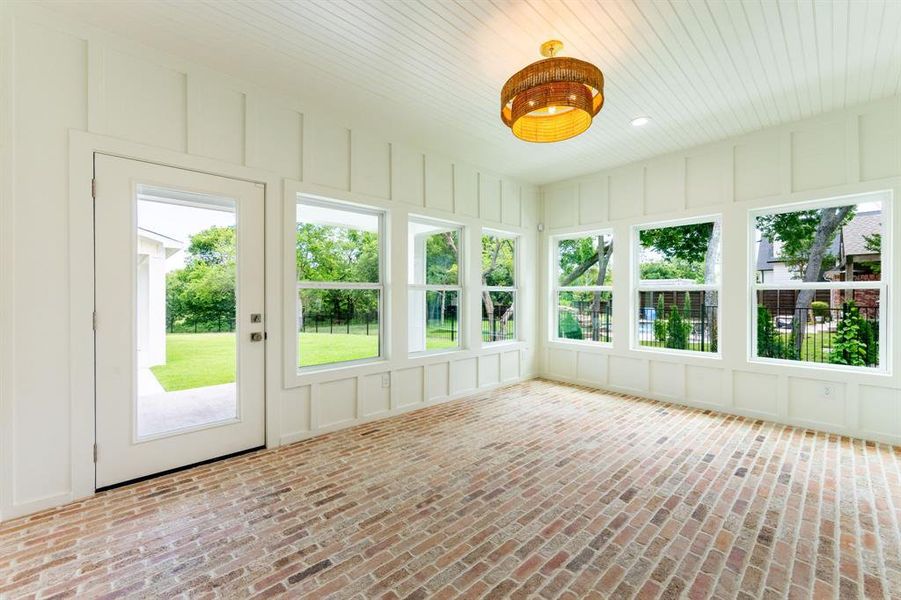 Sunroom featuring brick flooring, full-light exterior door, multiple windows, beadboard ceiling, and a decorative pendant light fixture Sunroom featuring brick flooring, full-light exterior door, multiple windows, beadboard ceiling, and a decorative pendant light fixture