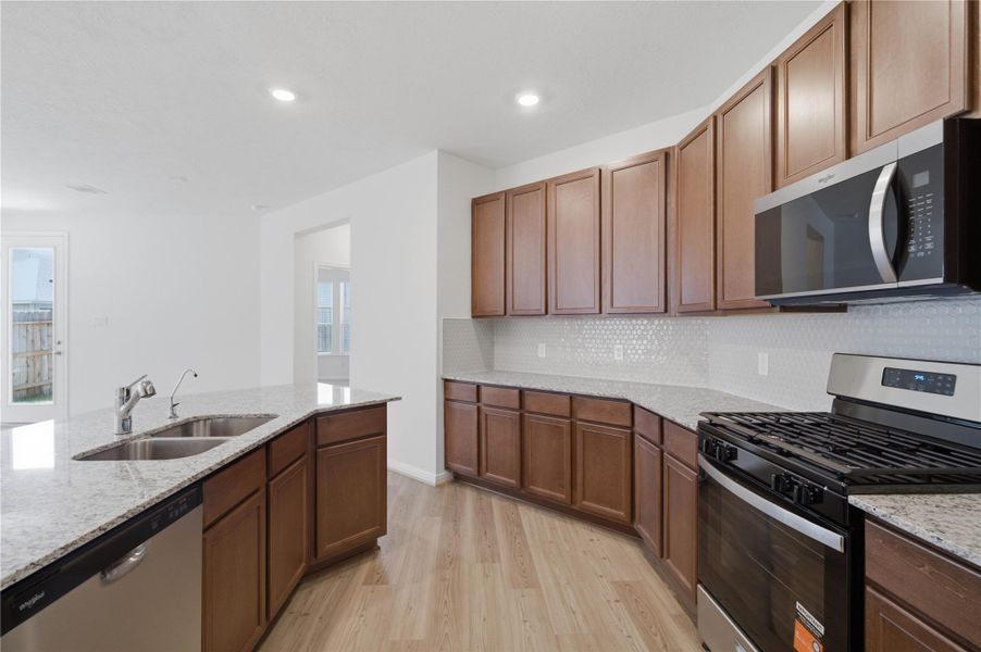 A true chef’s dream, this expansive kitchen boasts high ceilings, Woodmont Cody cabinets in Ginger stain, granite countertops in White Napoli, stainless steel appliances, a modern tile backsplash, recessed lighting, an island with a double sink, and a walk-in pantry—all with a clear view of the spacious Great Room. A true chef’s dream, this expansive kitchen boasts high ceilings, Woodmont Cody cabinets in Ginger stain, granite countertops in White Napoli, stainless steel appliances, a modern tile backsplash, recessed lighting, an island with a double sink, and a walk-in pantry—all with a clear view of the spacious Great Room.