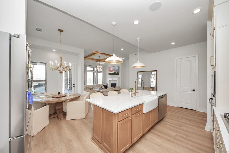 Bright and inviting open-concept kitchen and living area featuring a large island with a farmhouse sink, elegant pendant lighting, and a cozy dining nook with a modern chandelier.