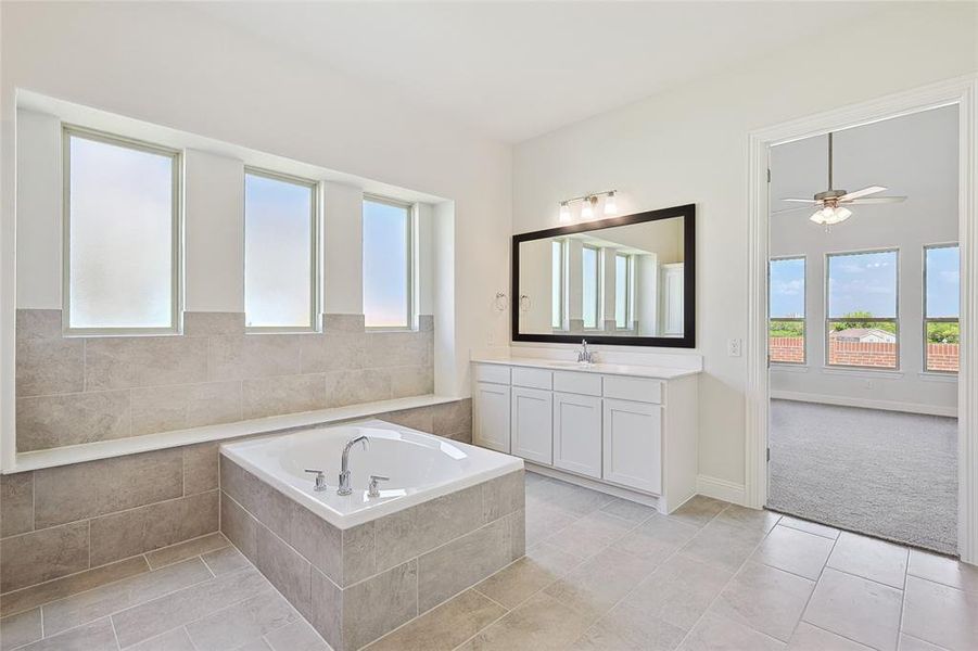 Bathroom with tiled bath, ceiling fan, vanity, and tile patterned floors