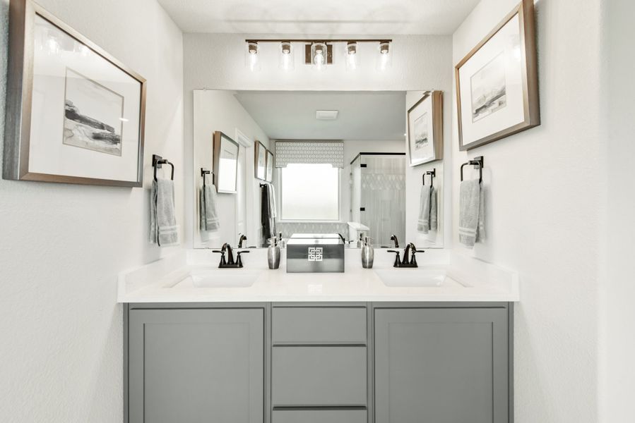Bathroom with double sink vanity, gray cabinets, white countertop, and large mirror with overhead lighting