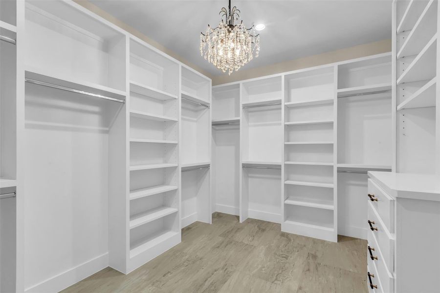 Spacious walk-in closet with custom white shelving, ample storage, and a stylish chandelier. Perfect for organizing and enhancing any wardrobe.