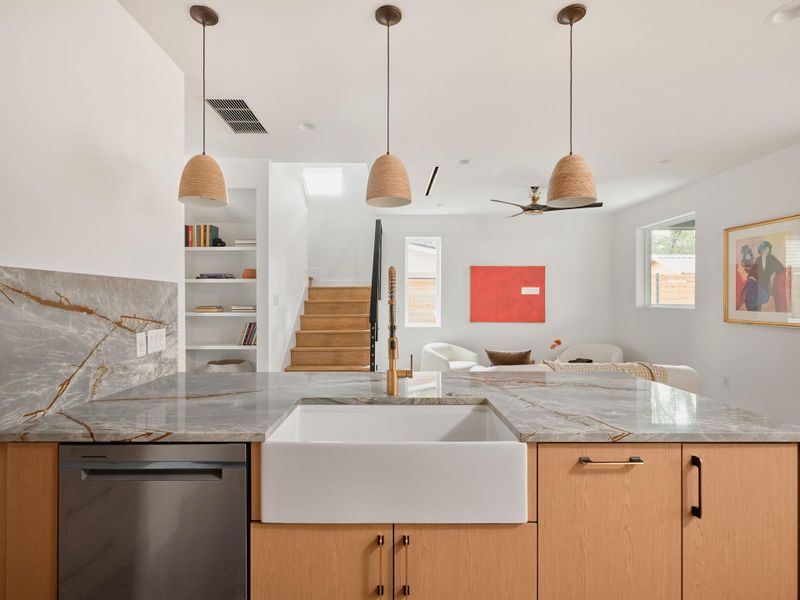 Kitchen featuring light brown cabinetry, light stone counters, stainless steel dishwasher, open floor plan, and pendant lighting Kitchen featuring light brown cabinetry, light stone counters, stainless steel dishwasher, open floor plan, and pendant lighting