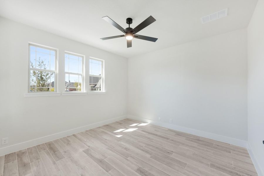 Empty bedroom with light wood-look floors, white walls, ceiling fan, and two windows with natural light