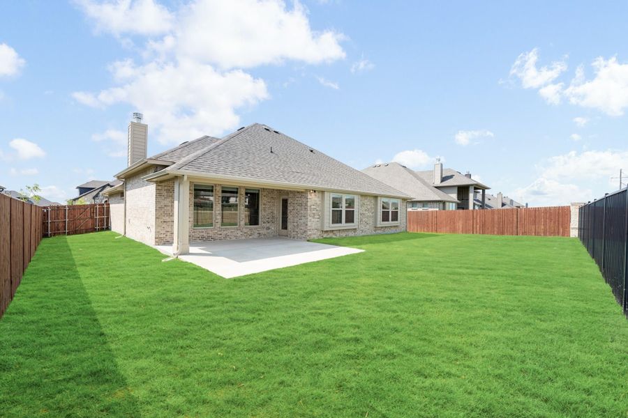 Brick home rear view with covered patio, large green lawn, and wood privacy fence