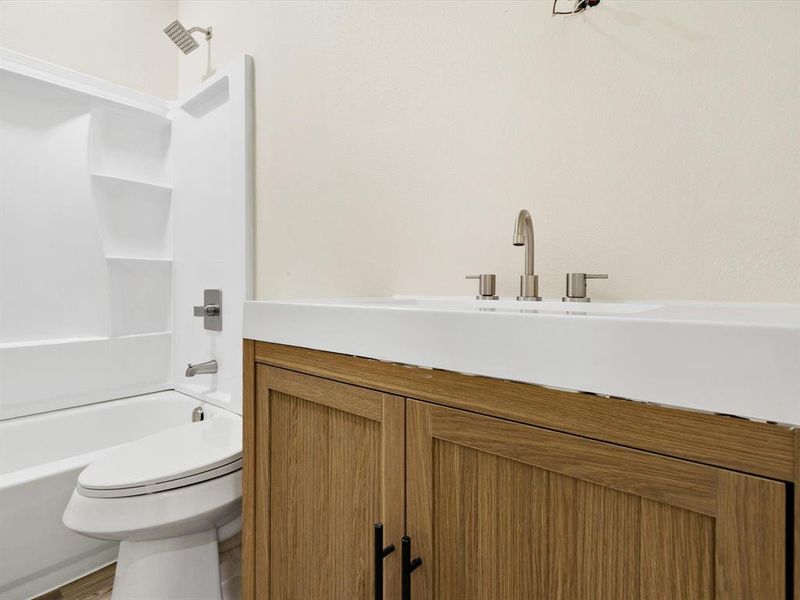 Bathroom vanity featuring a light wood-finish cabinet with black hardware, an integrated white sink, and a brushed nickel faucet Bathroom vanity featuring a light wood-finish cabinet with black hardware, an integrated white sink, and a brushed nickel faucet