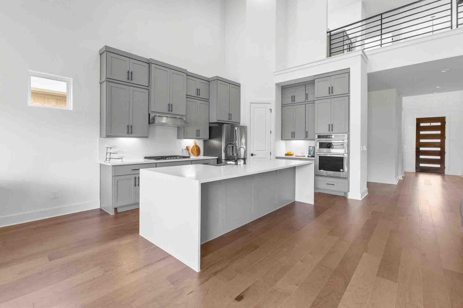 Kitchen featuring a central island with white countertop, grey cabinetry, stainless steel appliances, and wood-finish flooring