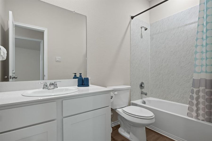 Full bathroom featuring shower / bath combo with shower curtain, vanity, and dark wood-style floors Full bathroom featuring shower / bath combo with shower curtain, vanity, and dark wood-style floors