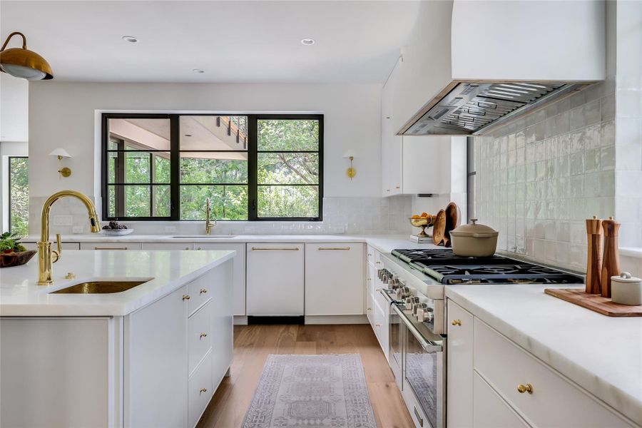 Bright kitchen featuring white cabinetry, light countertops, gold-tone hardware and fixtures, stainless steel appliances, and wood-finish flooring