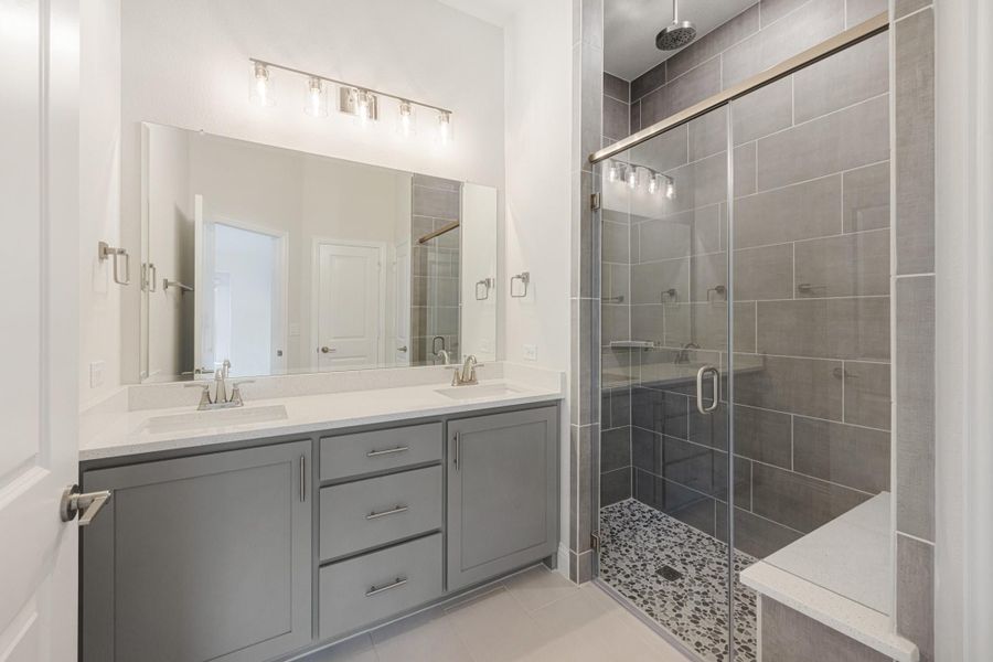 Bathroom with double-sink gray vanity, large mirror, and walk-in glass shower with gray tile and bench seat Bathroom with double-sink gray vanity, large mirror, and walk-in glass shower with gray tile and bench seat