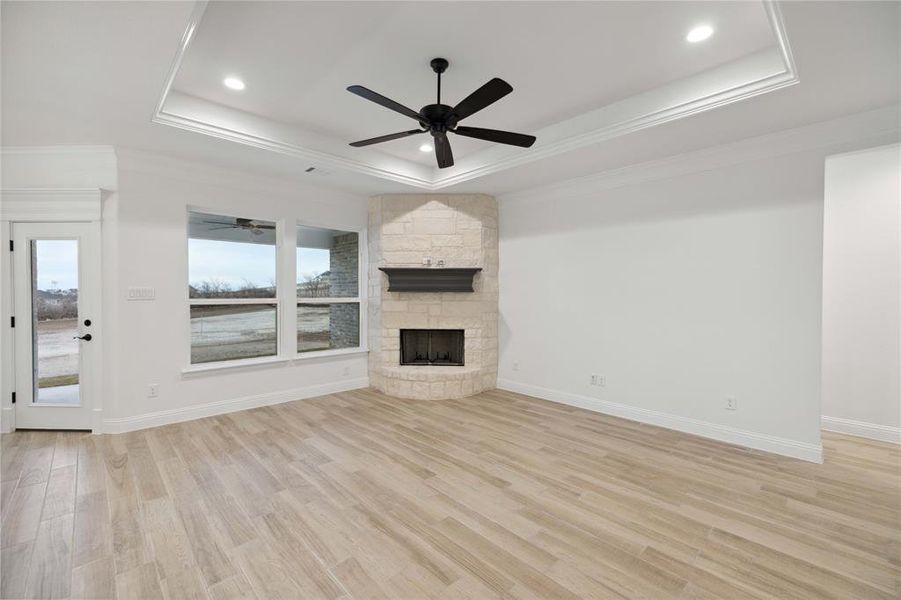 Unfurnished living room featuring a stone fireplace, a tray ceiling, ornamental molding, and light hardwood / wood-style flooring