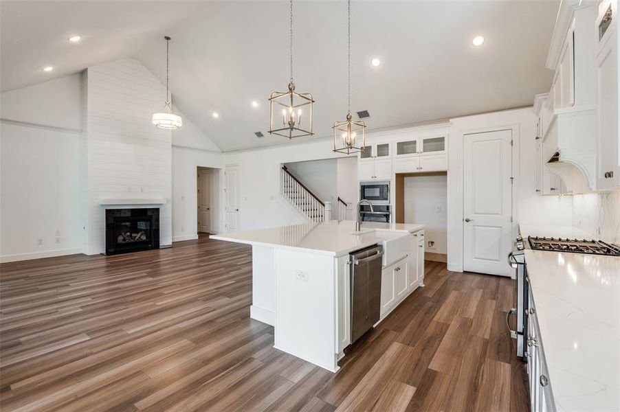 Kitchen featuring a center island with sink, white cabinetry, open floor plan, high vaulted ceiling, and light stone counters Kitchen featuring a center island with sink, white cabinetry, open floor plan, high vaulted ceiling, and light stone counters