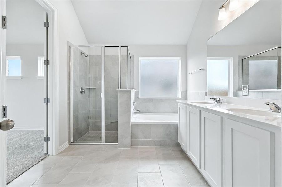 Bathroom with vaulted ceiling, a bath, a stall shower, double vanity, and tile patterned floors
