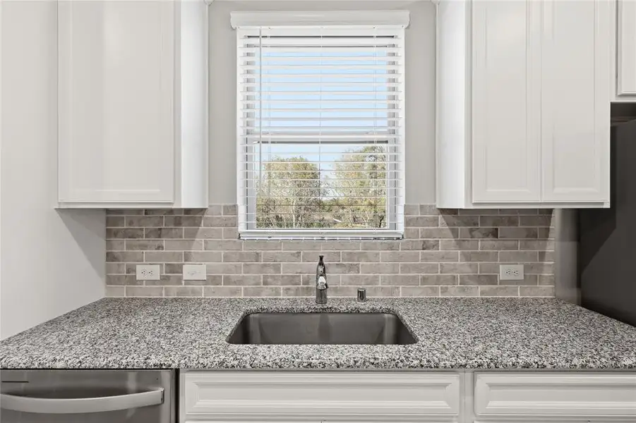 Kitchen featuring a stainless steel undermount sink with a chrome faucet, granite countertops, and a brick-patterned tile backsplash