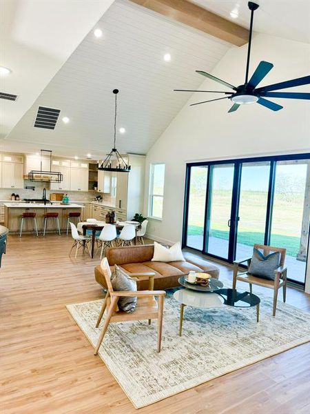 Living room with beamed ceiling, ceiling fan, high vaulted ceiling, and light hardwood / wood-style flooring