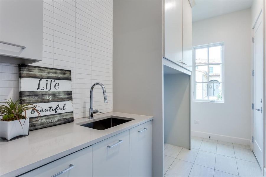 Kitchen featuring sink, white cabinets, light tile patterned floors, and backsplash