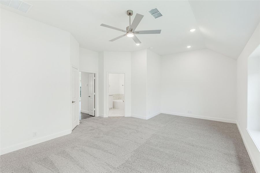 Empty bedroom with gray carpet, vaulted ceiling, ceiling fan, and open ensuite bathroom door Empty bedroom with gray carpet, vaulted ceiling, ceiling fan, and open ensuite bathroom door