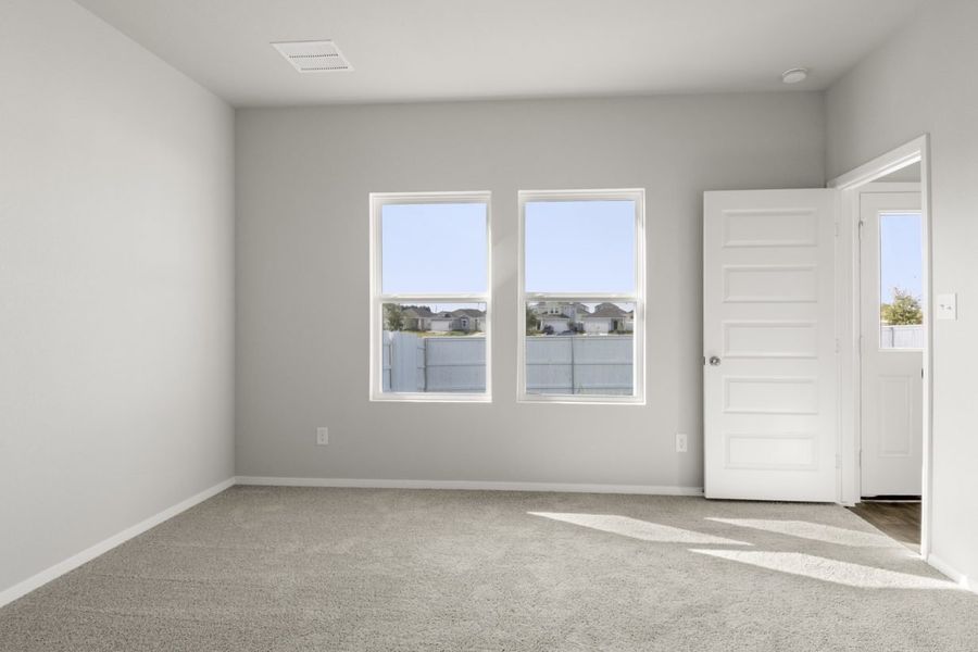 Image of primary bedroom with tan carpet and light grey walls and two windows