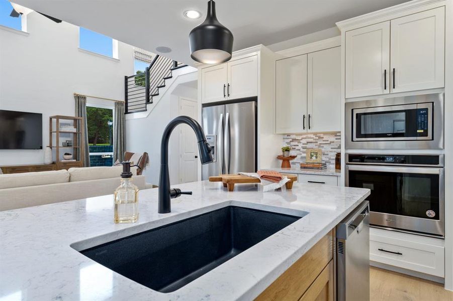 Kitchen with tasteful backsplash, light stone countertops, appliances with stainless steel finishes, sink, and light hardwood / wood-style flooring