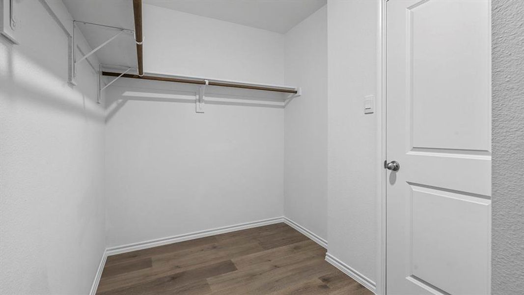 Spacious closet featuring durable wood-look flooring and a built-in hanging rod with shelving for organized storage
