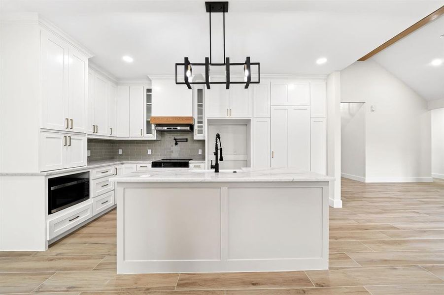 Modern kitchen featuring white cabinetry, a center island with a stone countertop, a built-in microwave, and wood-finish flooring Modern kitchen featuring white cabinetry, a center island with a stone countertop, a built-in microwave, and wood-finish flooring