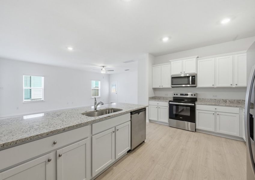 Kitchen featuring a granite island, white cabinetry, and stainless steel appliances open to the living space. Kitchen featuring a granite island, white cabinetry, and stainless steel appliances open to the living space.