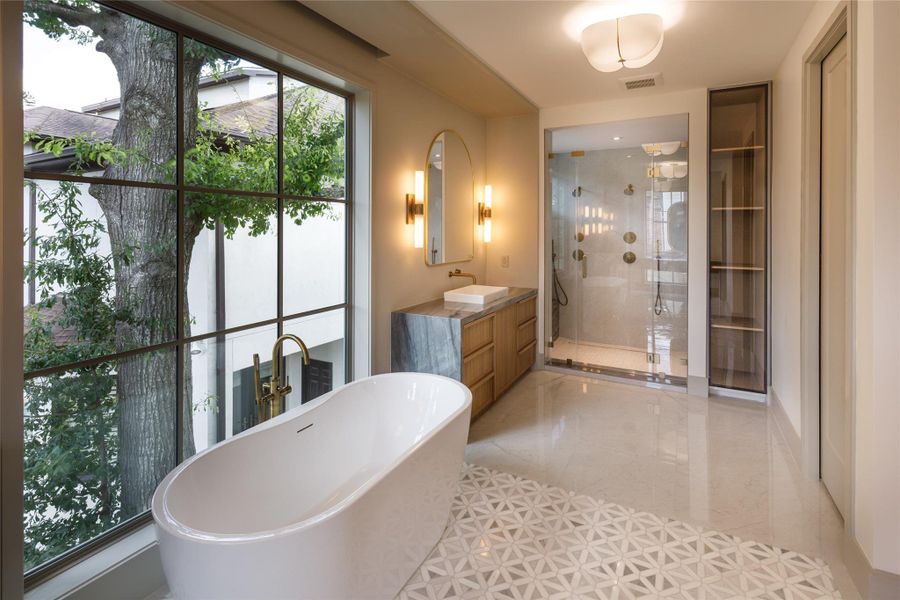Floor-to-ceiling glass brings the outdoors into the primary bath, while the soaking tub, oversized shower, warm wood cabinetry, and built-in storage make the space as functional as it is beautiful.