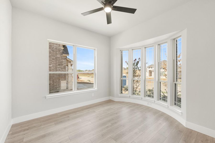 Empty room with bay windows, ceiling fan, and light hardwood floors overlooking a new neighborhood Empty room with bay windows, ceiling fan, and light hardwood floors overlooking a new neighborhood