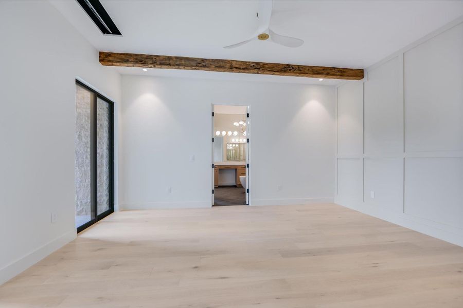 A spacious chamber presents a wood beam, recessed lighting, and access to an adjoining bathroom.