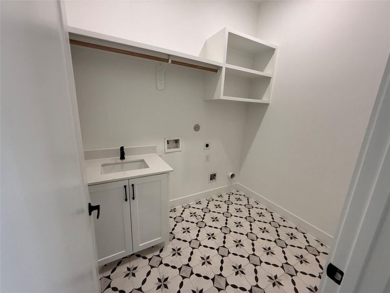 The second floor utility room features cabinetry, open shelving, and a patterned tile floor. It includes a space for a washer, dryer and  sink with storage.