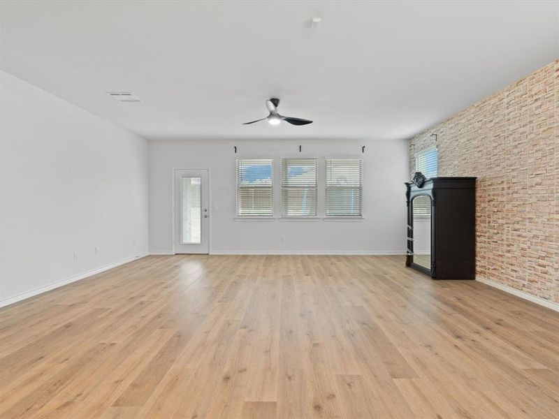 Unfurnished living room with a wealth of natural light, brick wall, and light wood-type flooring