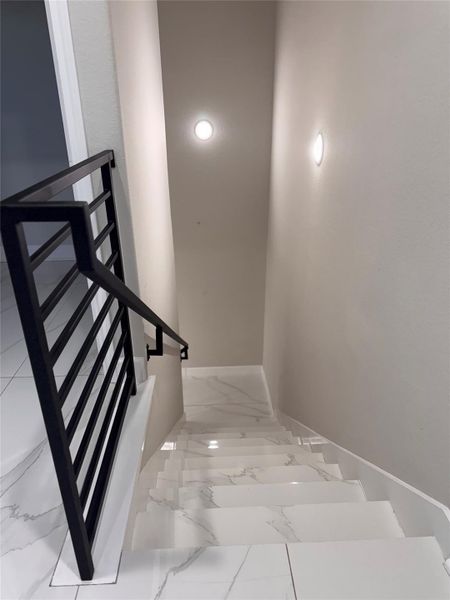 Sleek staircase with elegant white marble-look tiles and a modern black metal railing, illuminated by recessed lighting. Sleek staircase with elegant white marble-look tiles and a modern black metal railing, illuminated by recessed lighting.