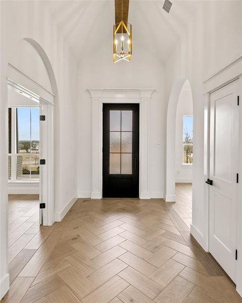 Entryway featuring wood-finish flooring in a herringbone pattern, a vaulted ceiling, and an ornate brass chandelier