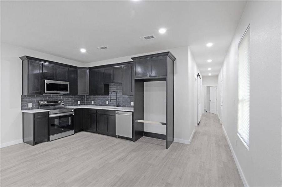 Kitchen with appliances with stainless steel finishes, tasteful backsplash, light hardwood / wood-style flooring, and sink