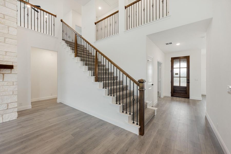 Two-story foyer with carpeted staircase, iron balusters, wood floors, and a wood front door with glass panels