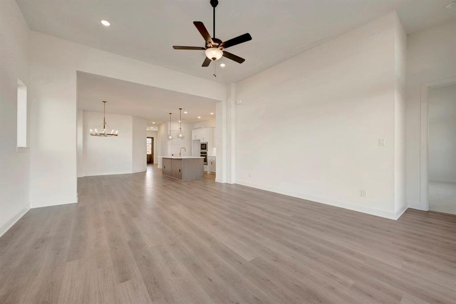 Unfurnished living room with a ceiling fan, a chandelier, and light wood-style floors Unfurnished living room with a ceiling fan, a chandelier, and light wood-style floors