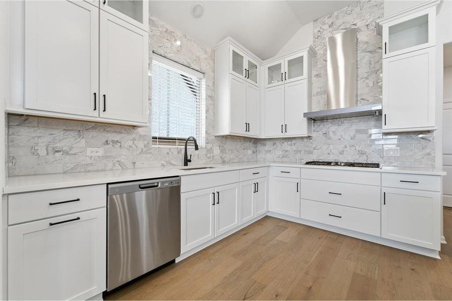 Modern kitchen featuring white cabinetry with black hardware, stainless steel appliances, light-toned countertops, and a full-height tile backsplash