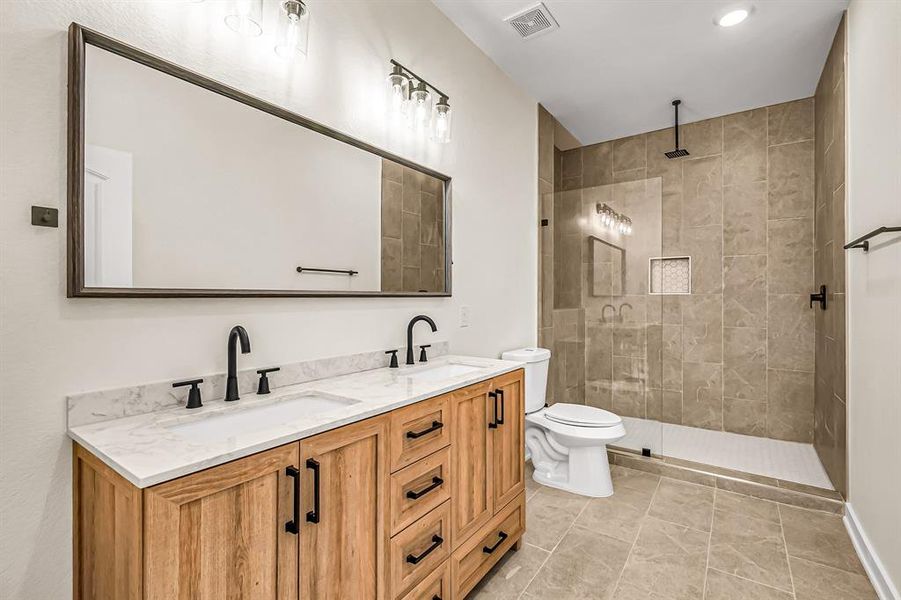 Double sinks in the primary bath with designer wood vanity. Seamless glass shower enclosure and attractive tile flooring and inset.