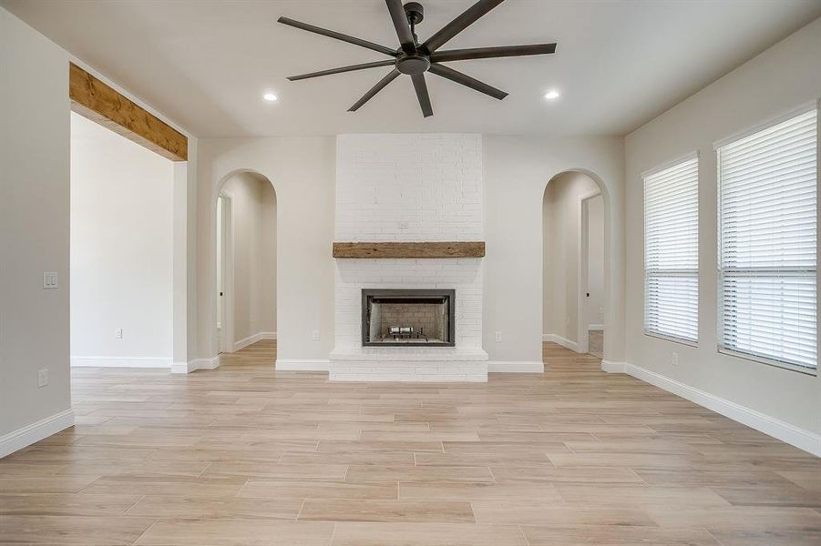 Unfurnished living room with light wood-style floors, a brick fireplace, arched walkways, recessed lighting, and ceiling fan Unfurnished living room with light wood-style floors, a brick fireplace, arched walkways, recessed lighting, and ceiling fan