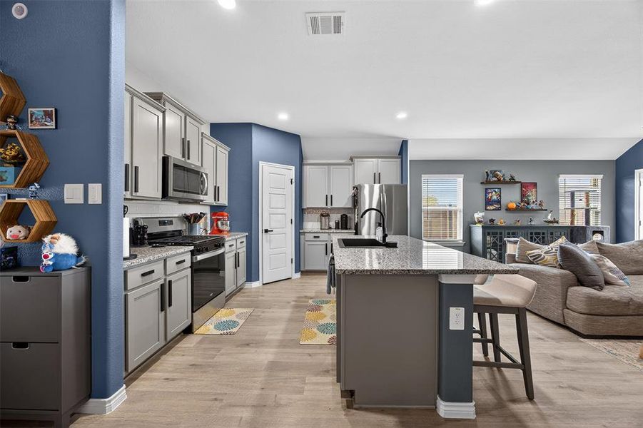 Kitchen featuring open floor plan, a breakfast bar, stainless steel appliances, light wood-style flooring, and a kitchen island with sink