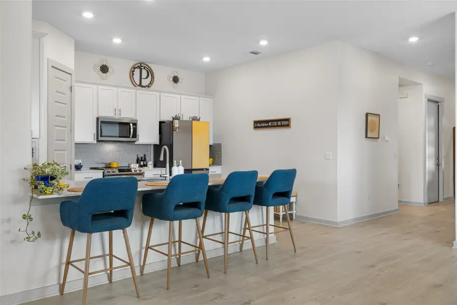 Kitchen featuring a kitchen bar, decorative backsplash, light wood finished floors, a peninsula, and white cabinetry Kitchen featuring a kitchen bar, decorative backsplash, light wood finished floors, a peninsula, and white cabinetry