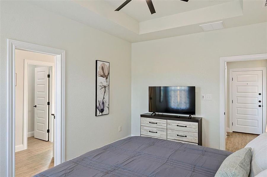 Recessed tray ceiling with ceiling fan, light-toned wall paint, and wood-finish flooring