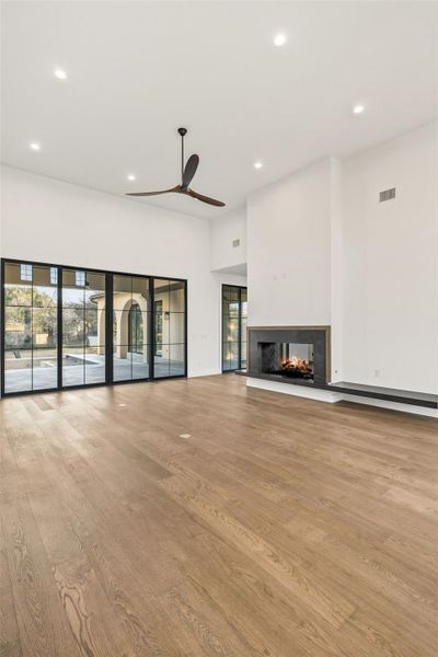 Unfurnished living room featuring light wood finished floors, a multi sided fireplace, a ceiling fan, recessed lighting, and a high ceiling