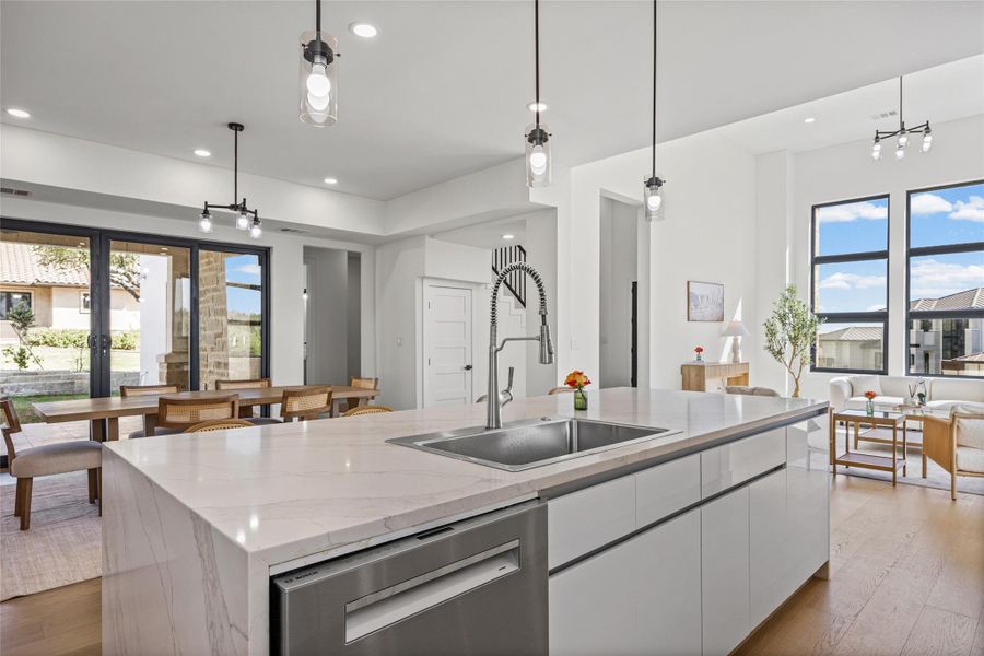 Kitchen featuring plenty of natural light, light wood-type flooring, light stone counters, and a kitchen island with sink