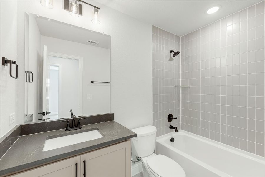 Bathroom with single vanity, dark countertop, toilet, and tub-shower combo with gray tile surround