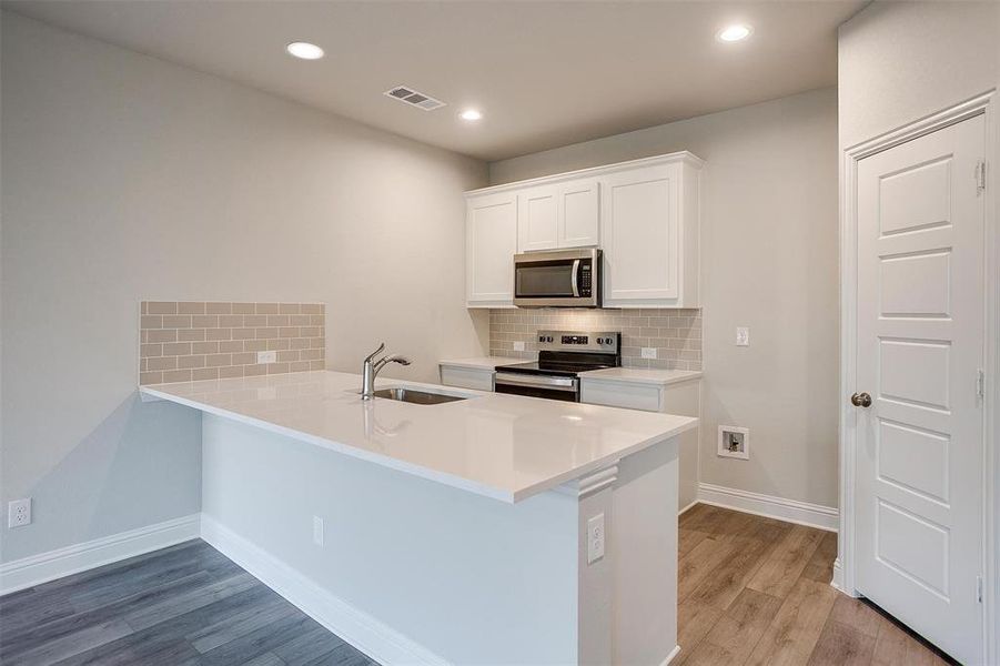 Kitchen with sink, white cabinetry, stainless steel appliances, kitchen peninsula, and light wood-type flooring