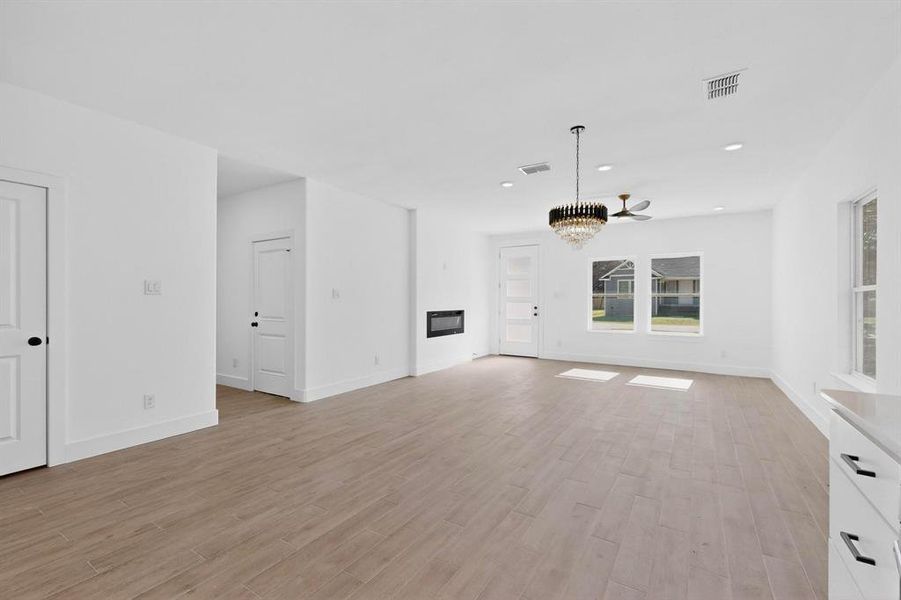 Unfurnished living room featuring light wood-style floors, recessed lighting, a glass covered fireplace, and a chandelier