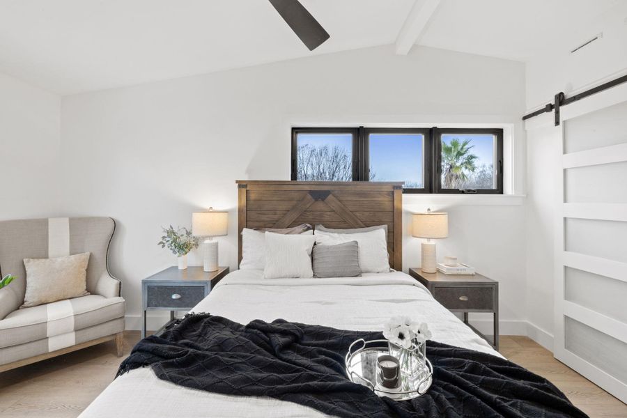 Bedroom with a ceiling fan, lofted ceiling with beams, a barn door, light wood finished floors, and baseboards